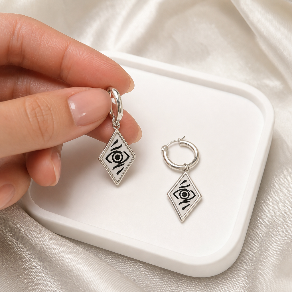 Hand holding CosNova silver diamond eye hoop earring beside matching earring on tray for scale