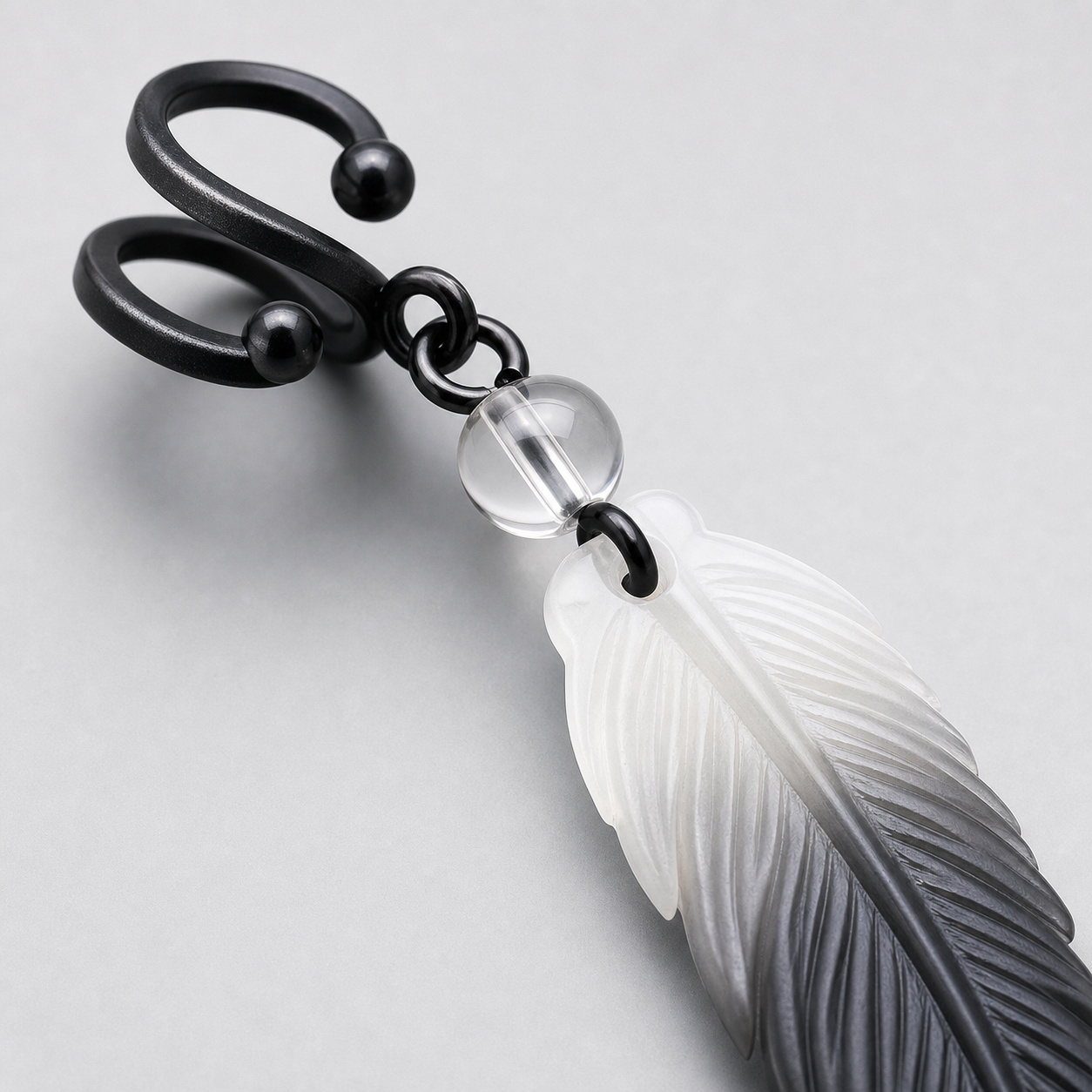 Macro detail of CosNova black adjustable ear cuff clear bead connector and engraved gradient resin feather
